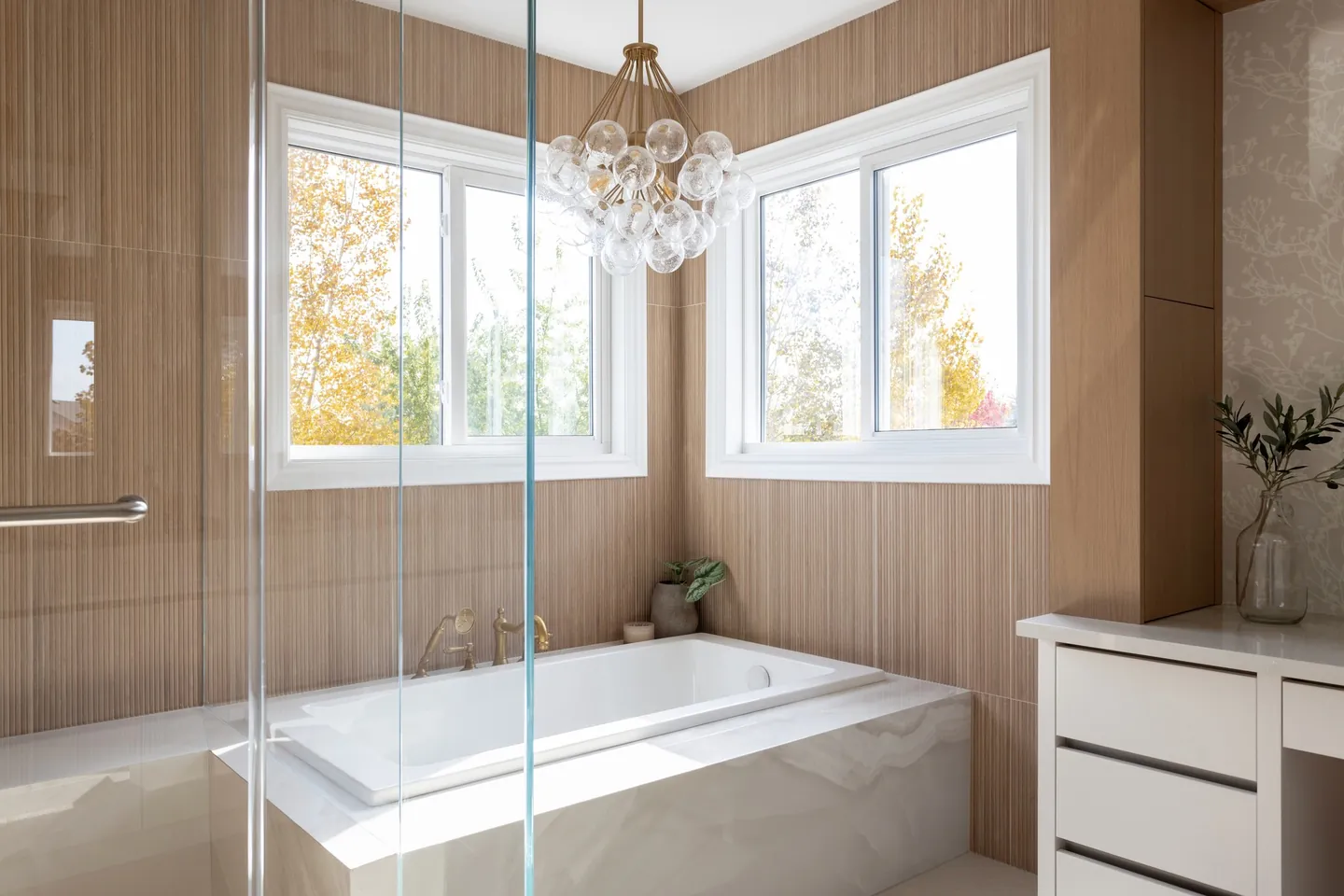 Freestanding tub beneath a crystal chandelier with vertical wood-look tile